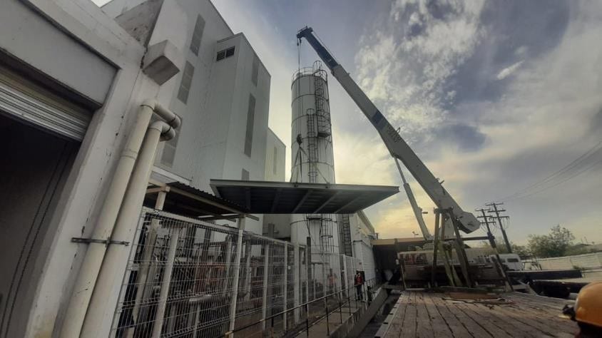 Maniobra de montaje con grúa: izaje de un silo y estructura de acero al atardecer