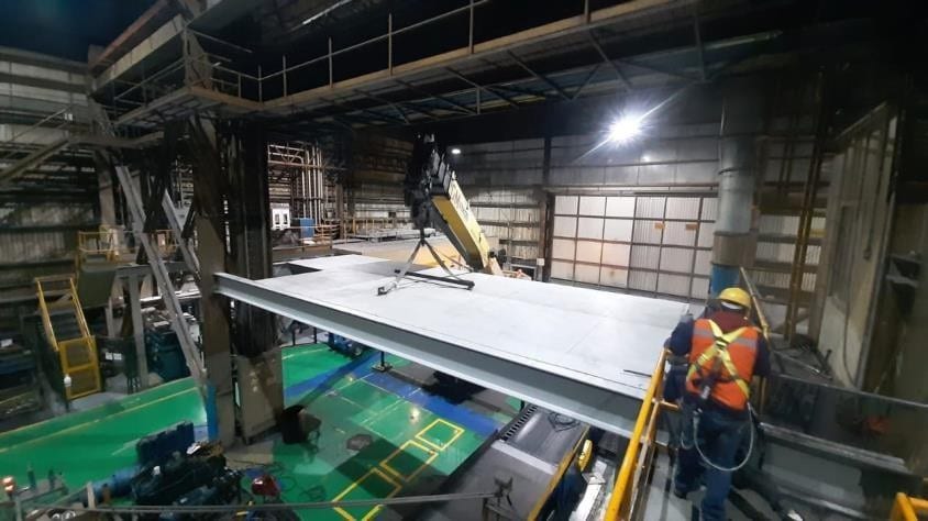 Puente grúa del taller izando un panel de acero mientras un operario lo guía