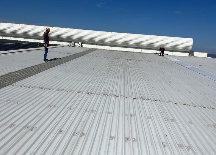 Operarios con arnés y línea de vida instalando lámina sobre una cubierta industrial